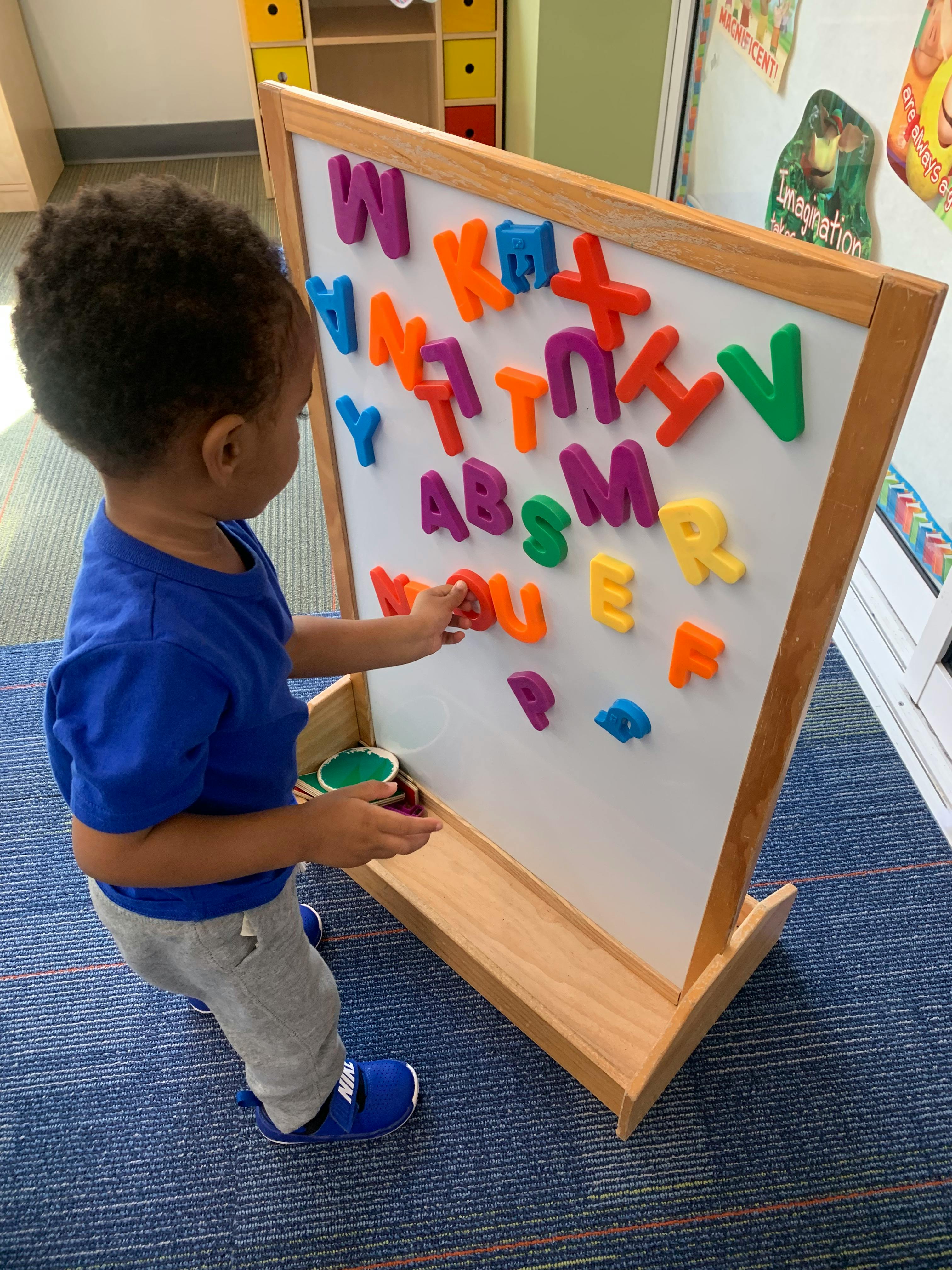 Child playing with magnetic letters on a whiteboard