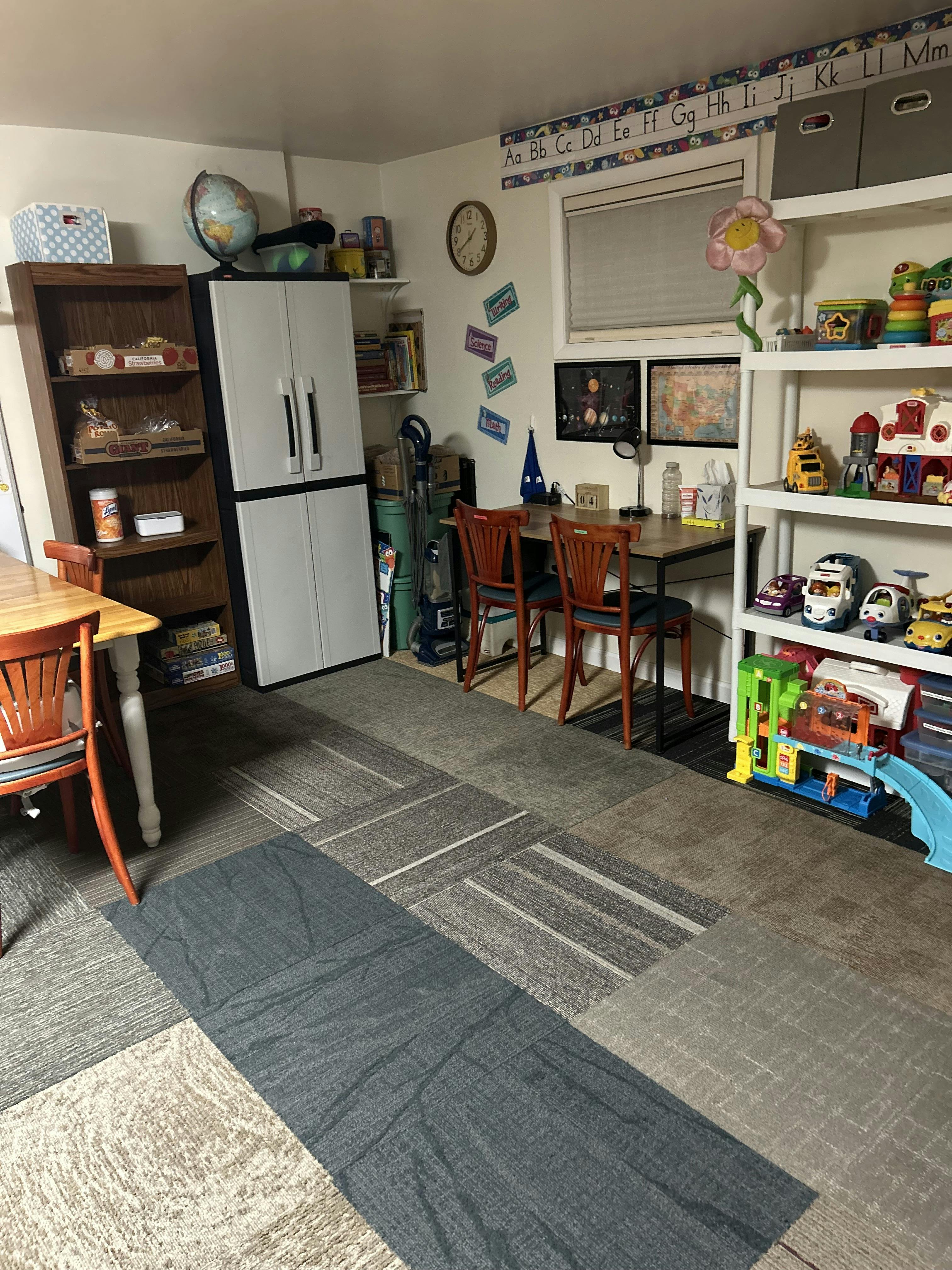 Classroom interior with desks, chairs, toy shelves, and educational wall charts