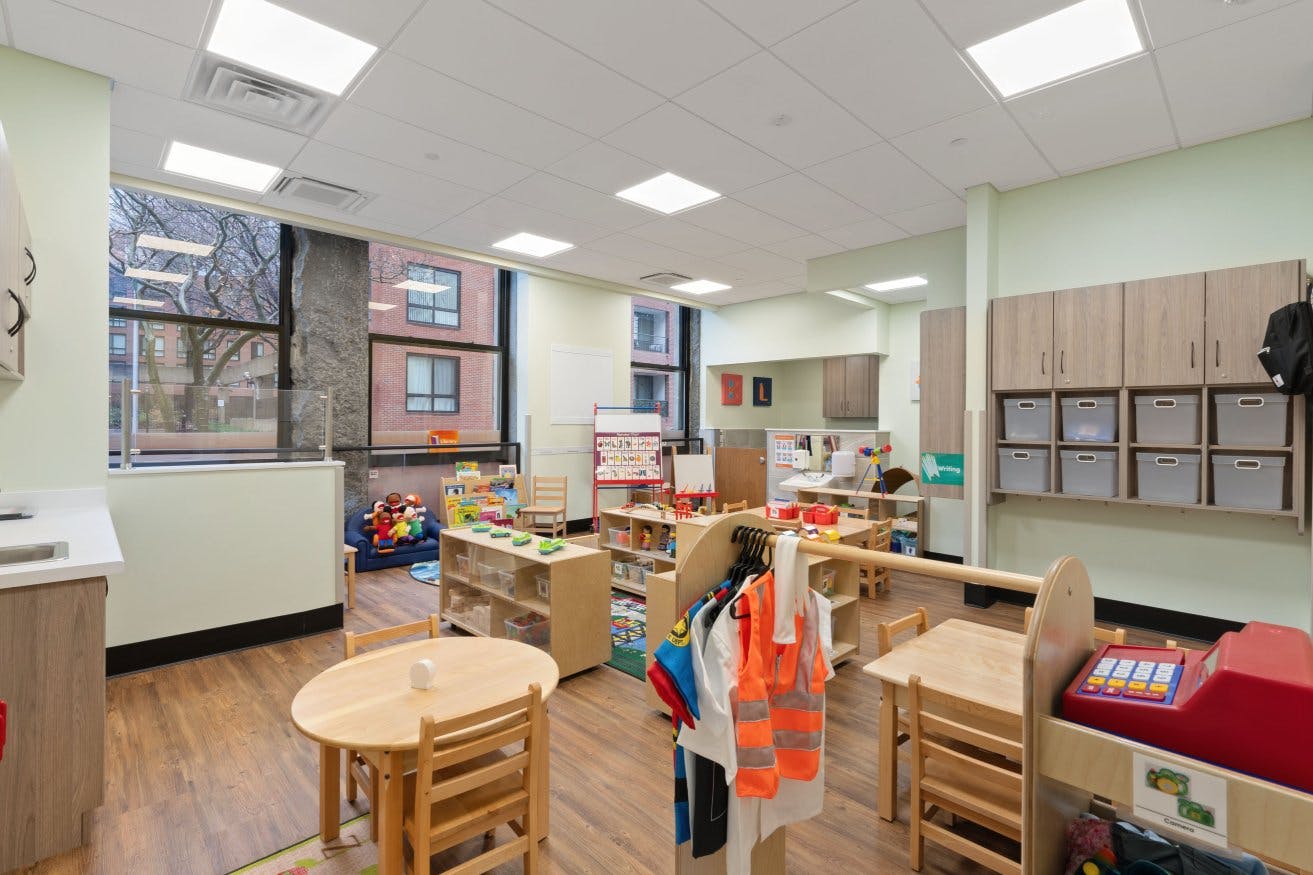 A classroom with small tables and chairs, play kitchen, and dress-up clothes