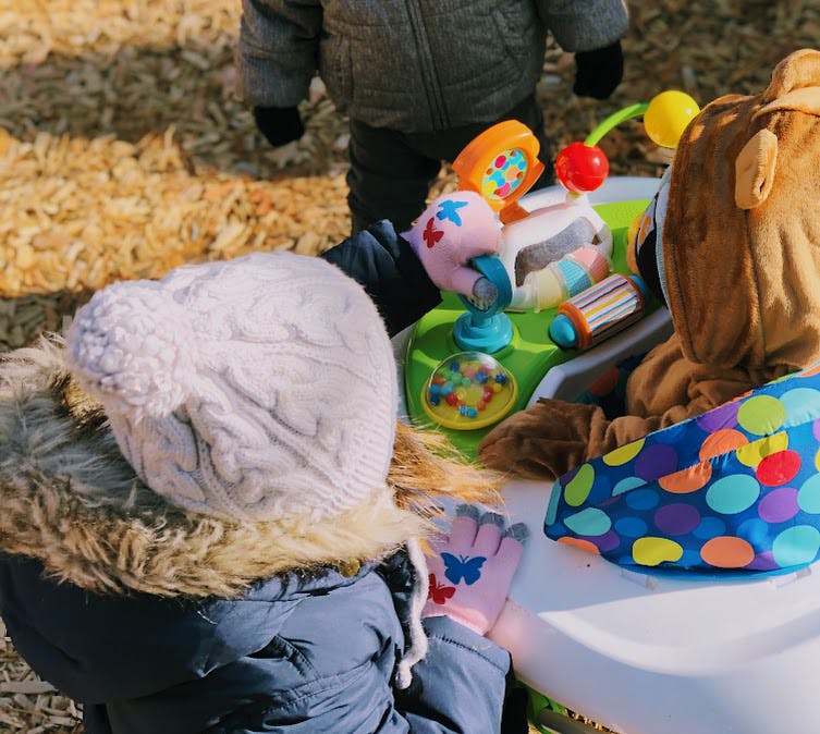 Child in winter coat and hat playing with a colorful activity toy