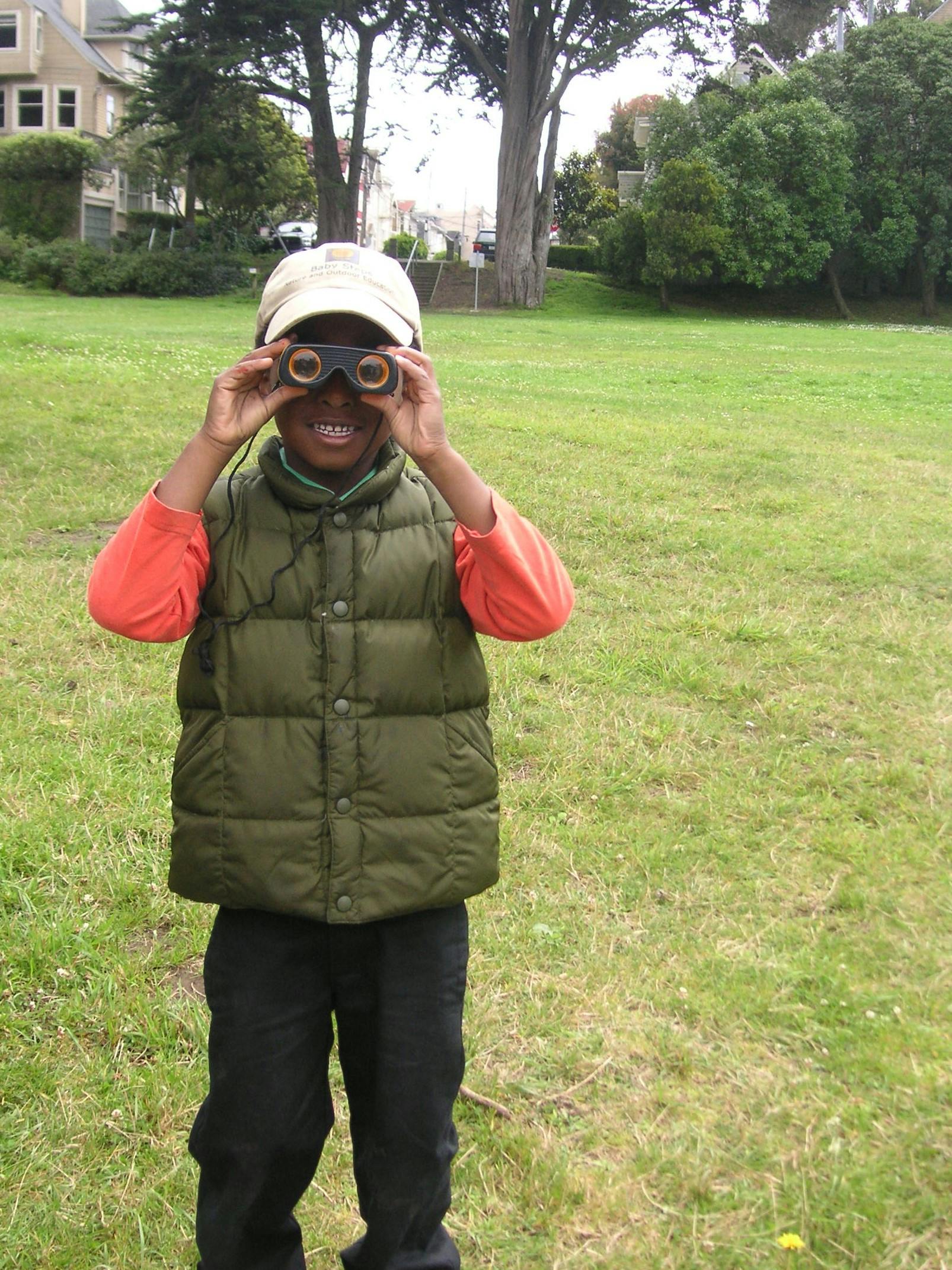 Child in a vest and cap looking through binoculars