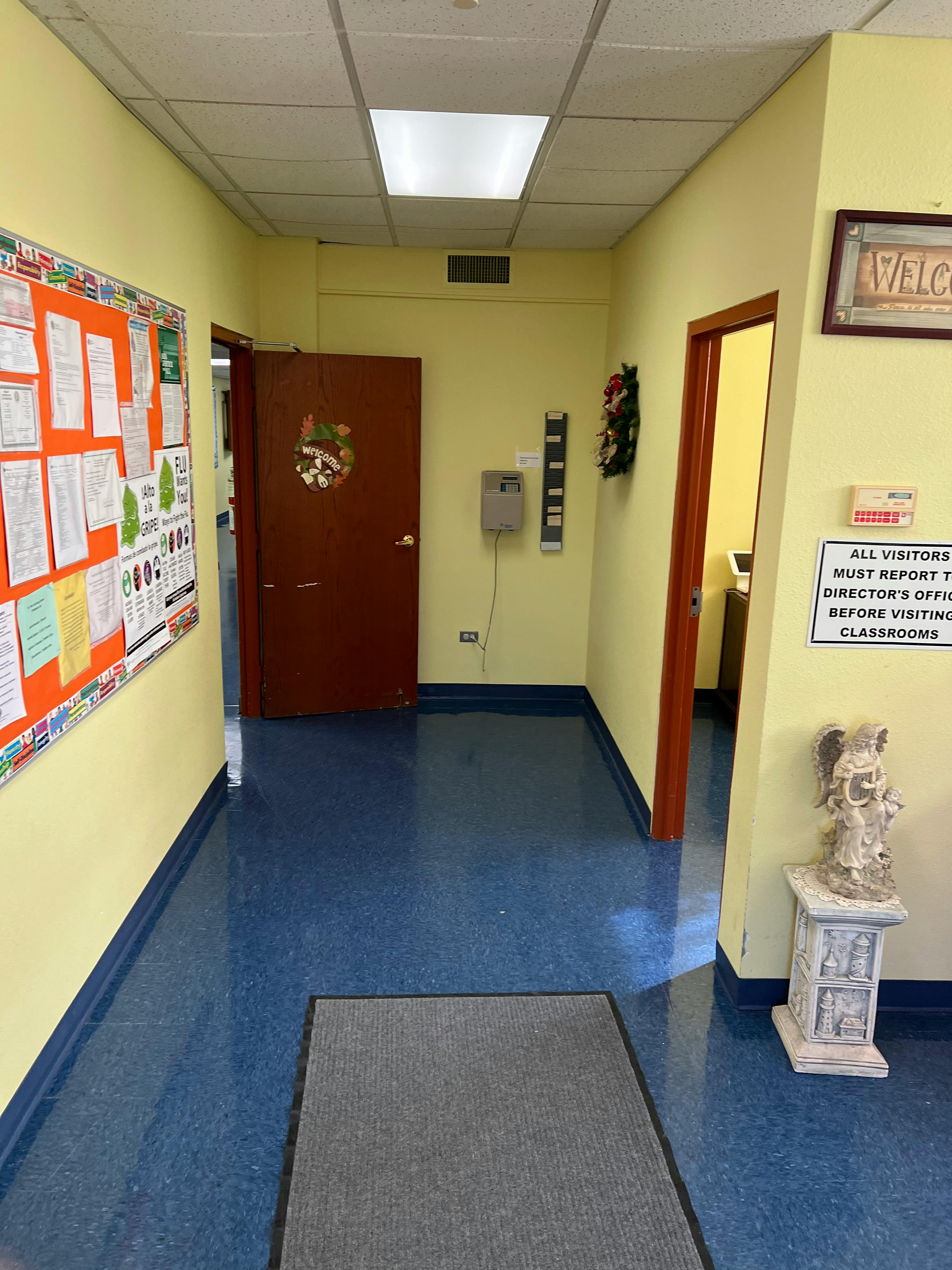 Hallway with bulletin board, two doors, and a sign about visitors