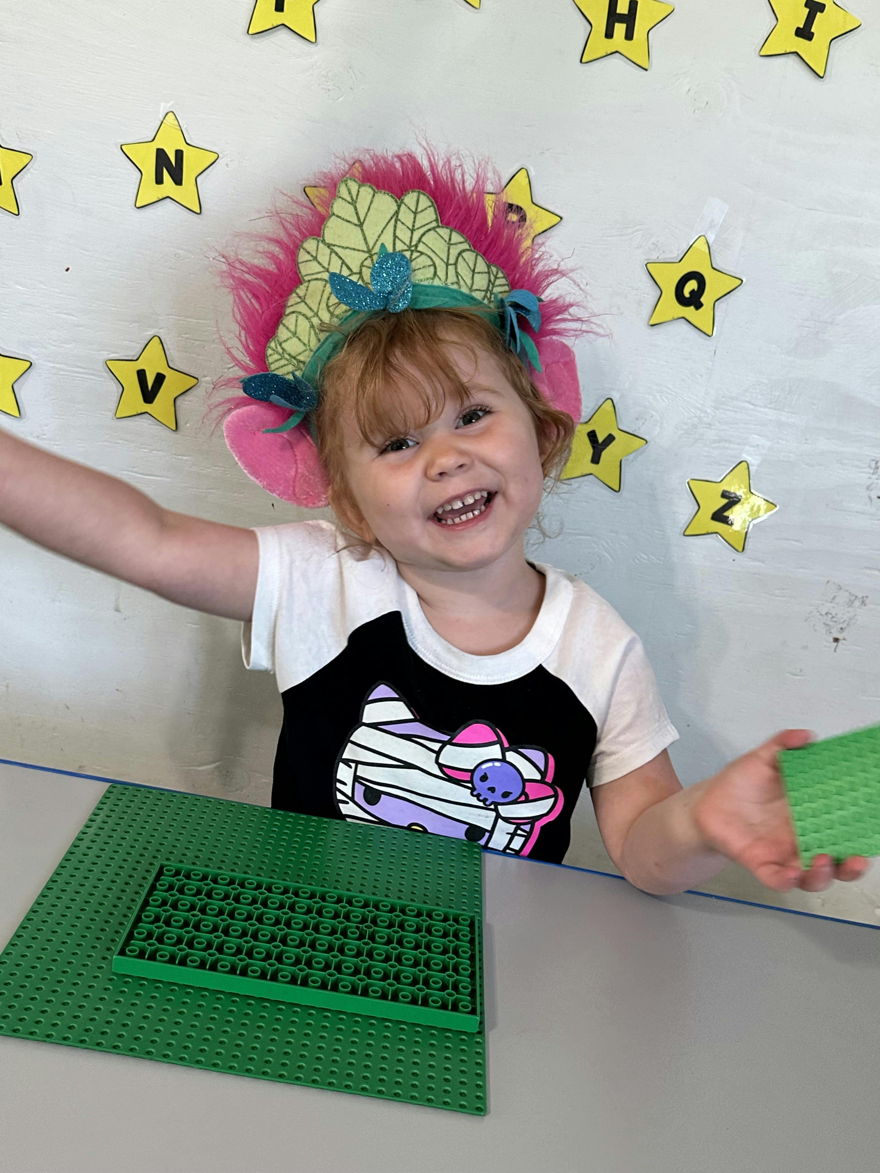 Child in a troll headband playing with green interlocking plastic bricks
