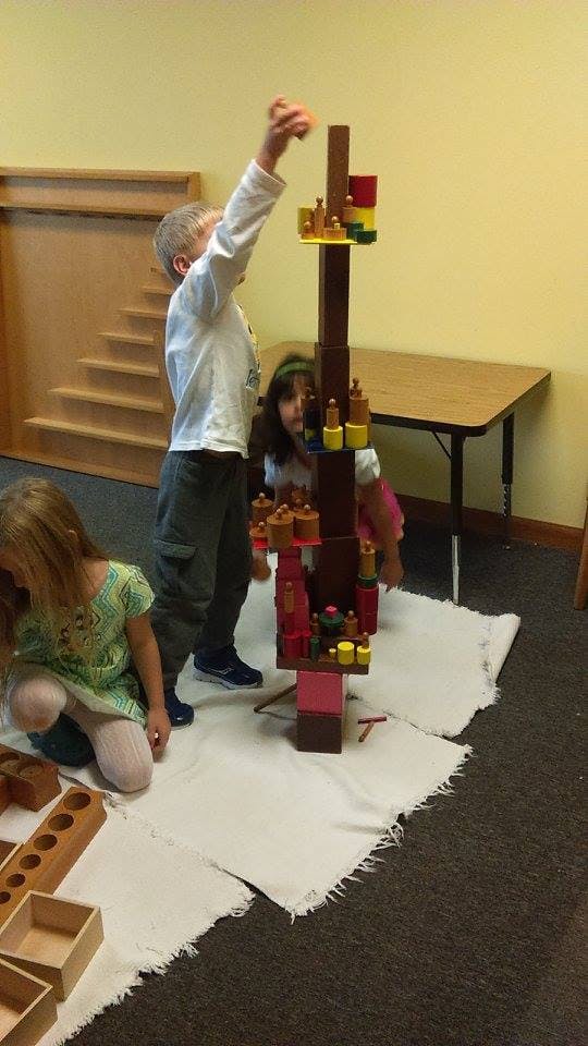 Child reaching up to place a block on a tall structure, another child watching