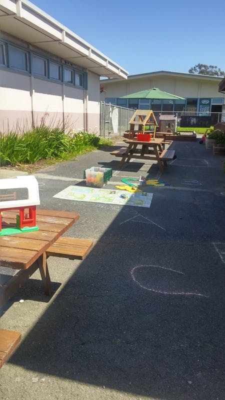Outdoor play area with picnic tables, toys, and chalk drawings on the ground