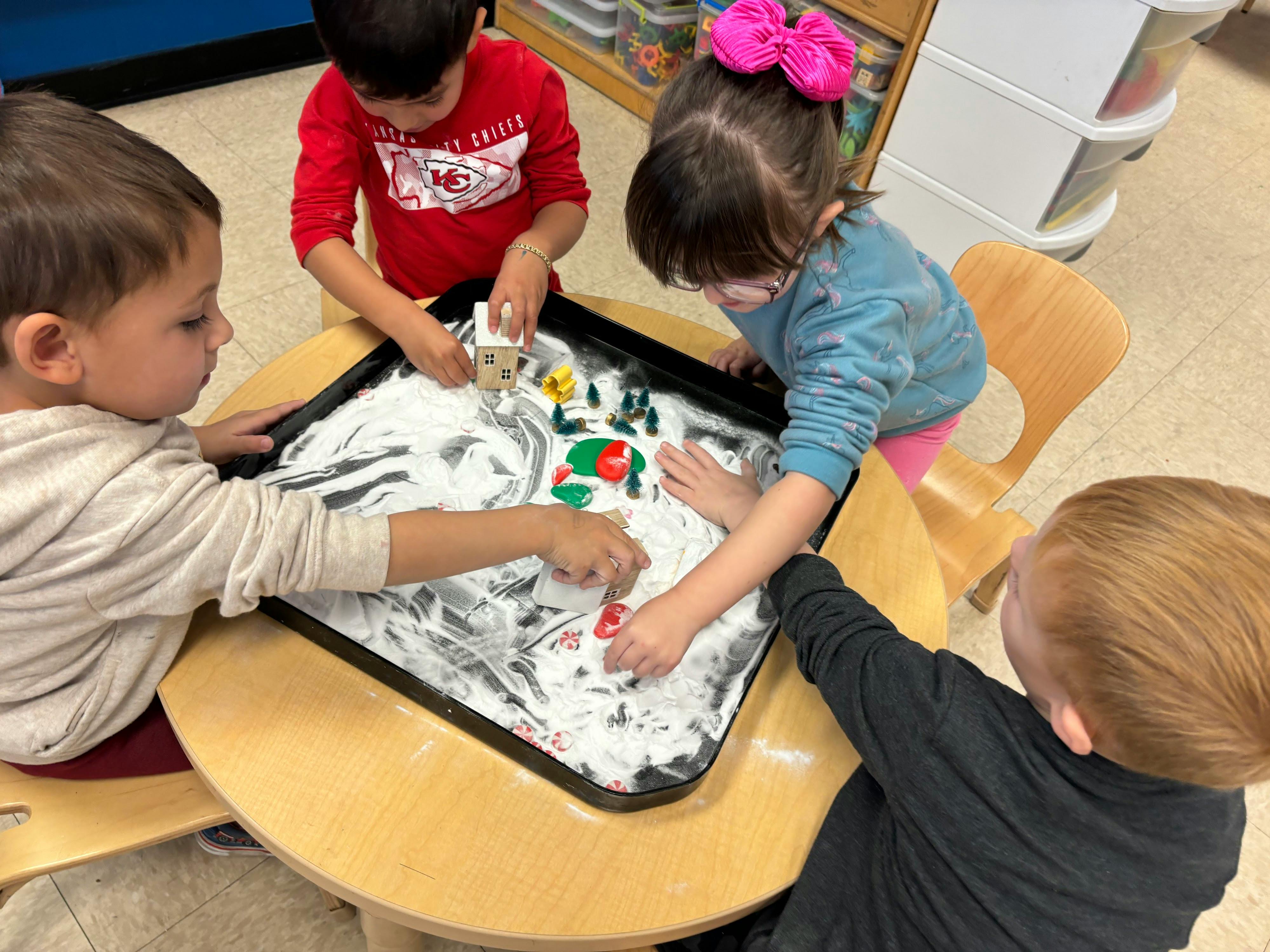 Children playing with shaving cream and small toys in a tray