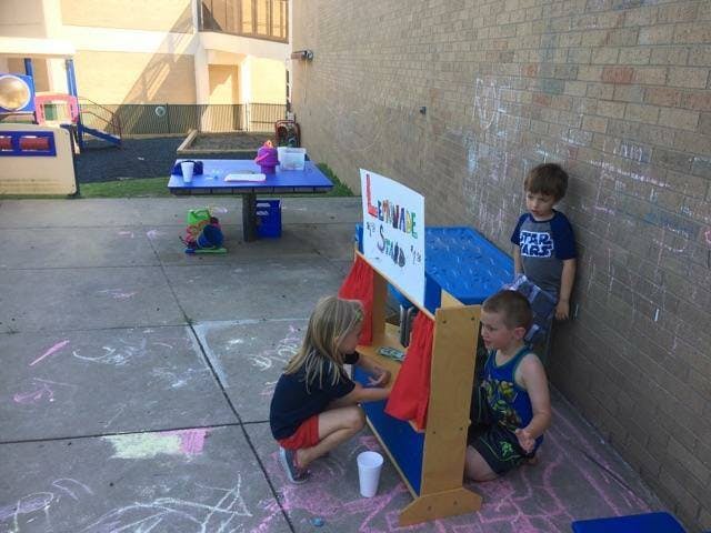 Three children playing at a stand with a sign that says "Lemonade & Snow"