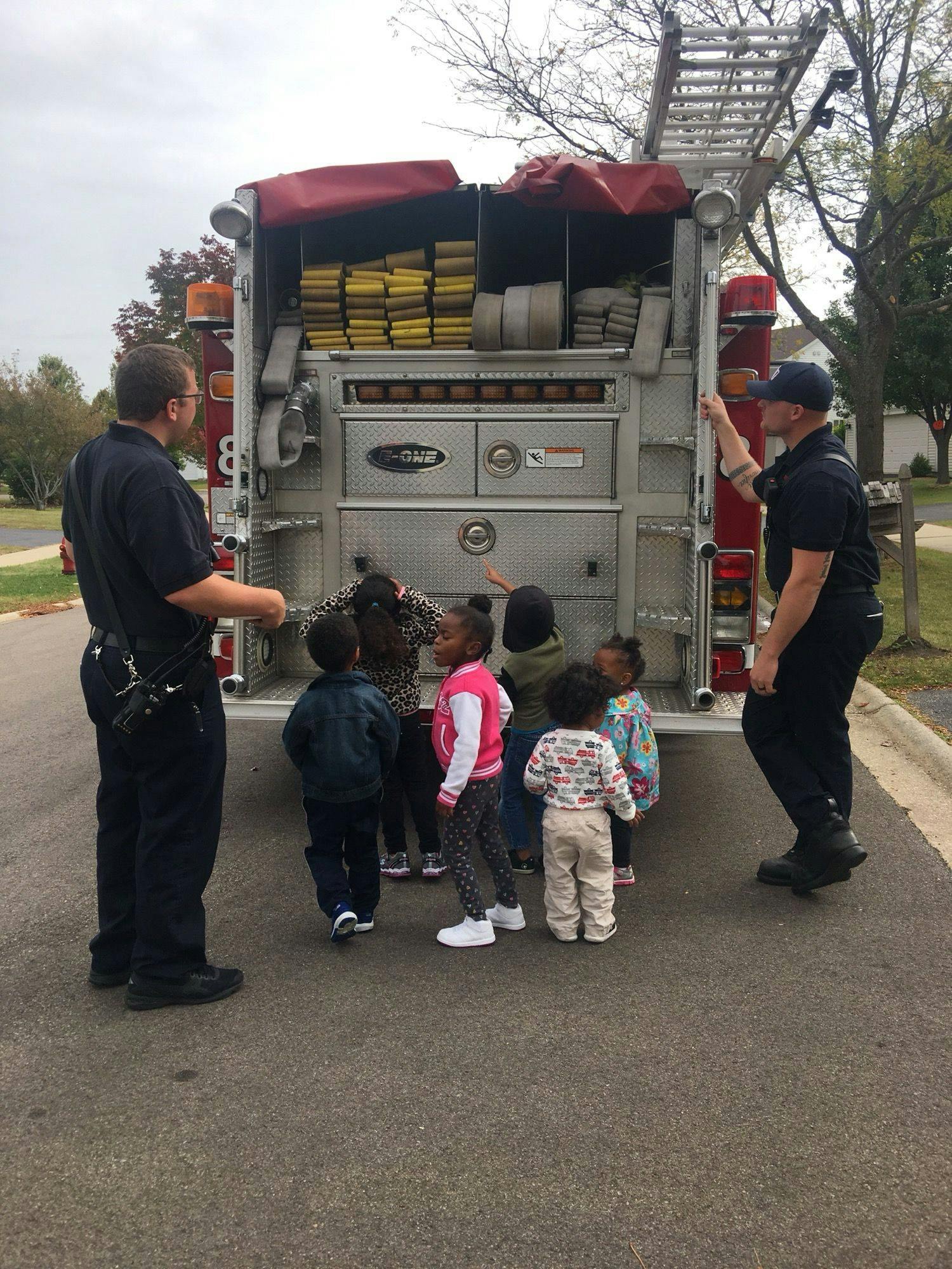 Two people and several children gathered around the back of a fire truck