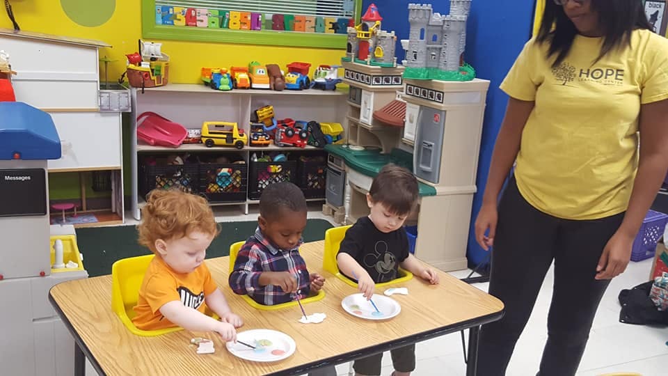 Adult standing near three children seated at a table with plates