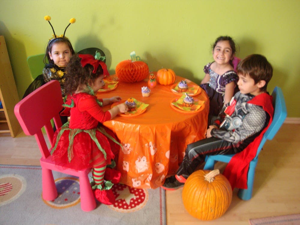 Four children in costumes sitting around a table with pumpkins