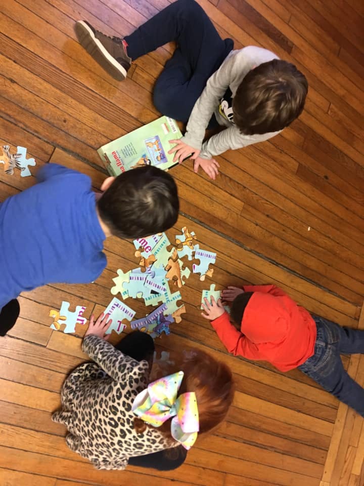 Four children on a wooden floor assembling a puzzle