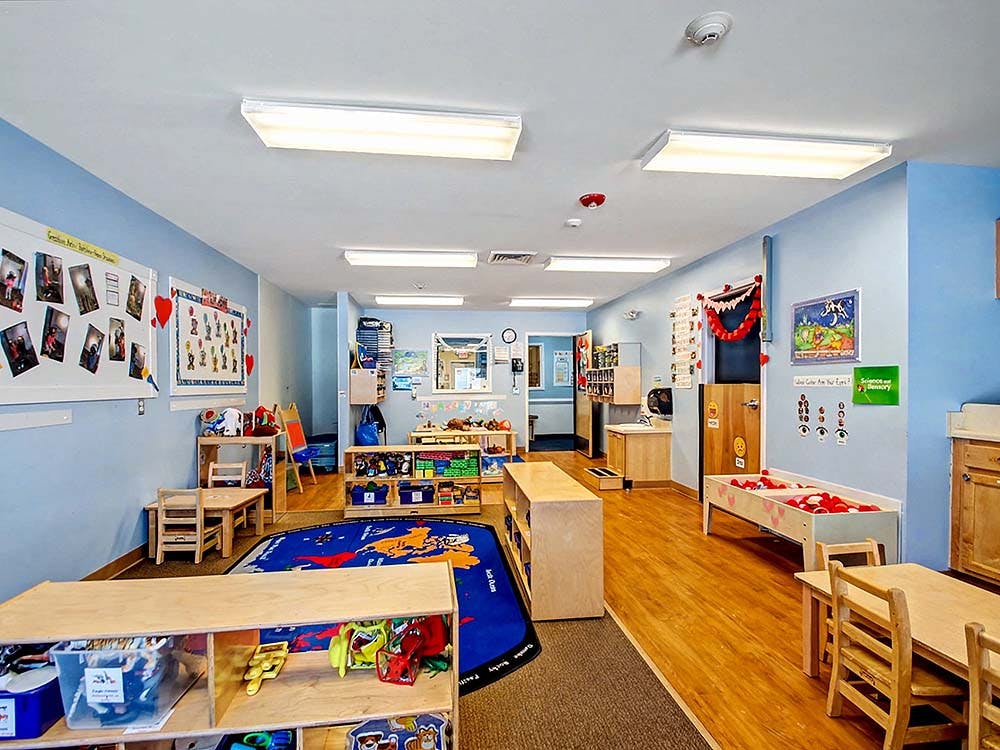 A colorful classroom with blue walls, small wooden tables, and a world map rug