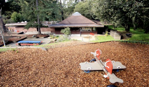 Playground with a toy airplane on wood chips and a building in the background