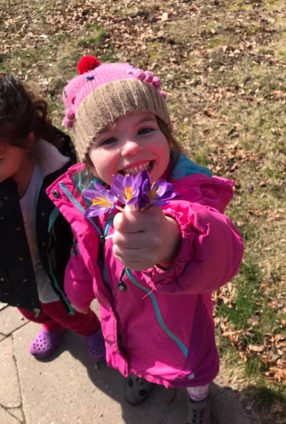 Child in a pink hat and jacket holding purple flowers