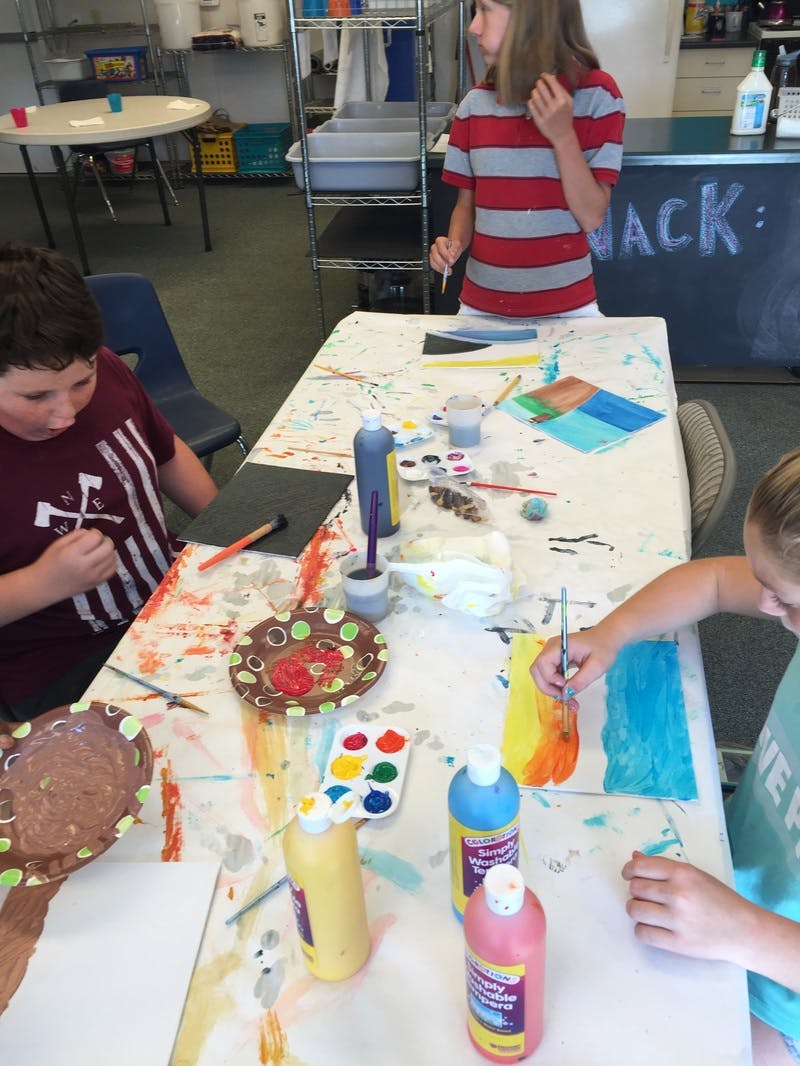 Three children painting at a table with art supplies