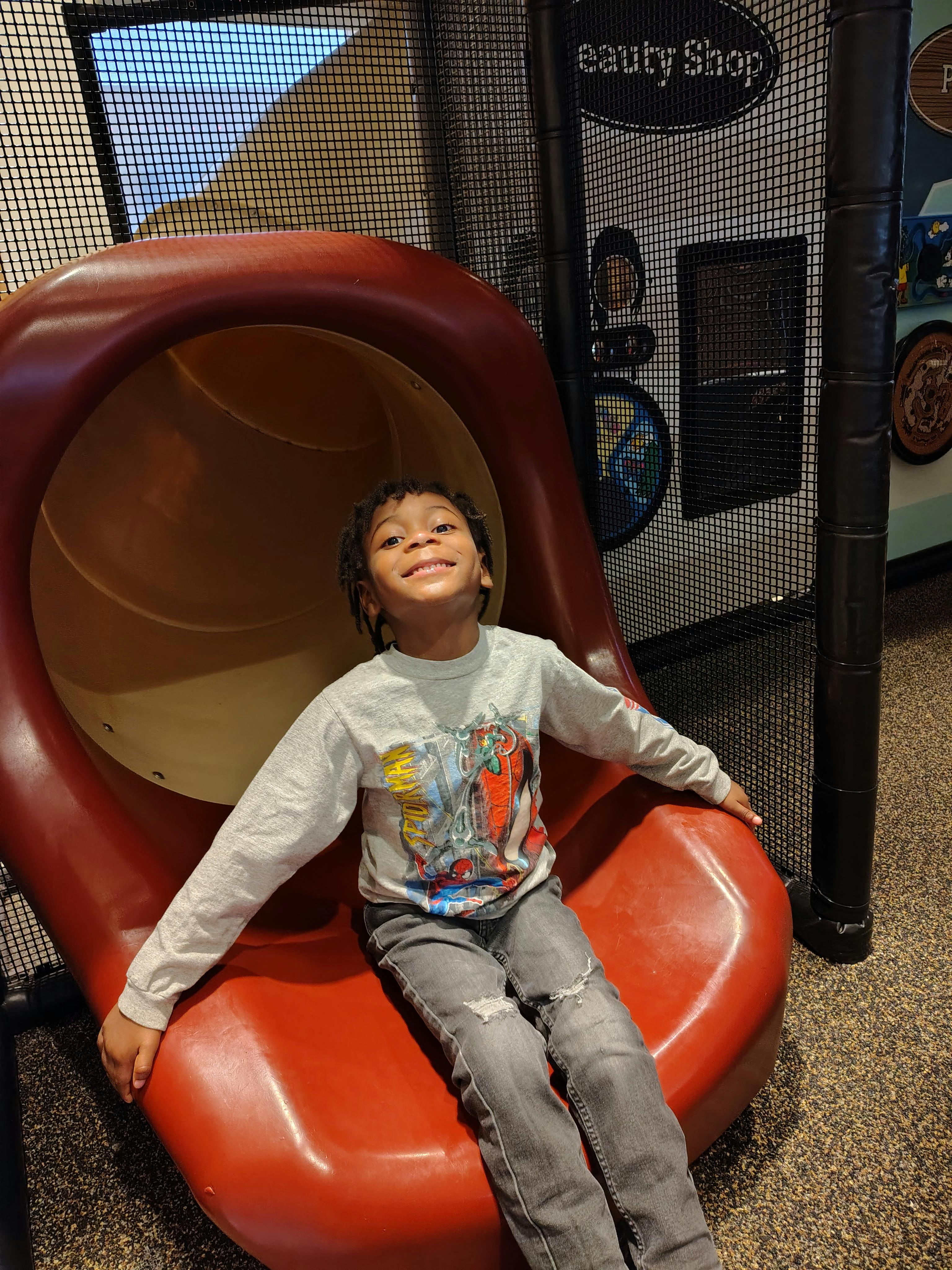Child lying on a red and tan slide, smiling up at the camera