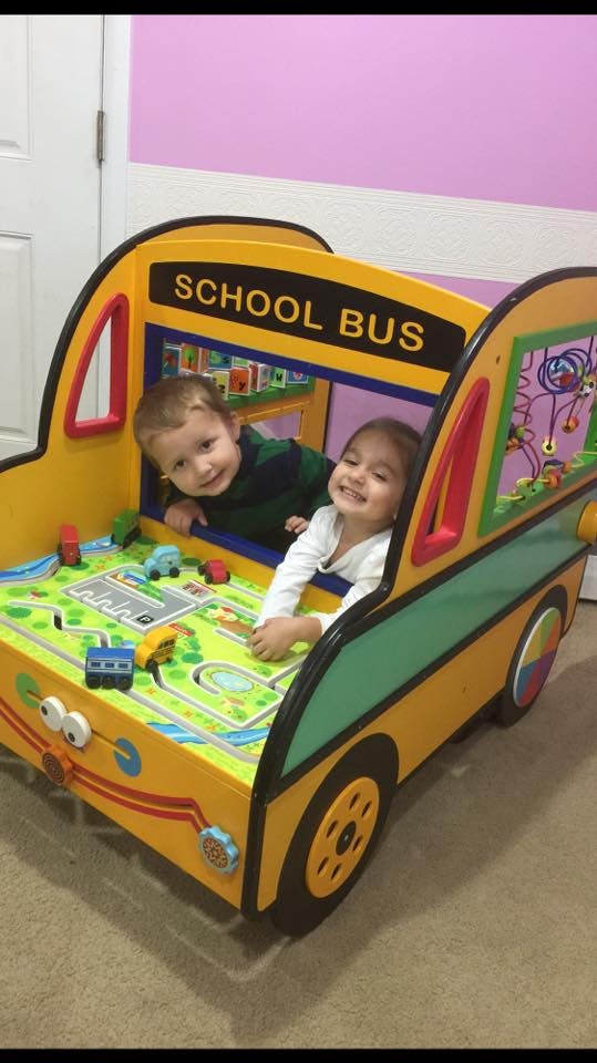Two children playing in a toy school bus with a play mat