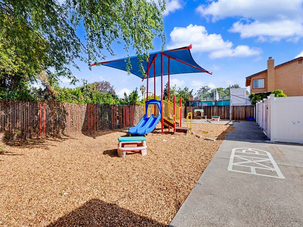Outdoor playground with a blue slide, climbing structure, and wood chips