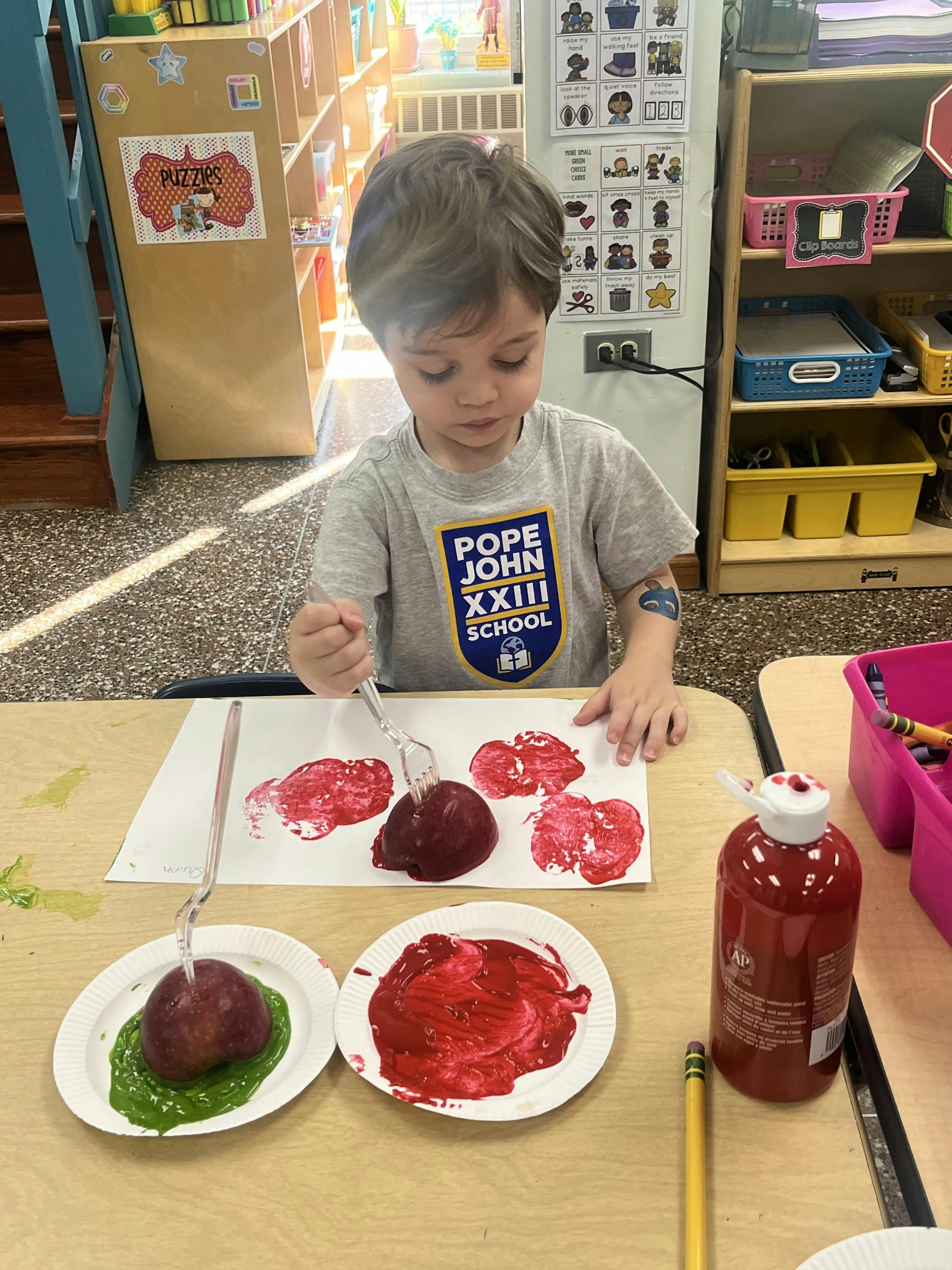 Child using a fork to stamp a red apple onto paper with red paint