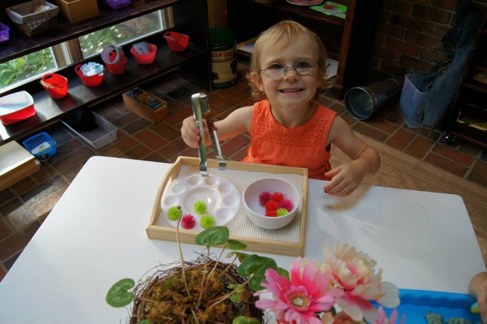 Child with glasses using tongs to move small pom-poms