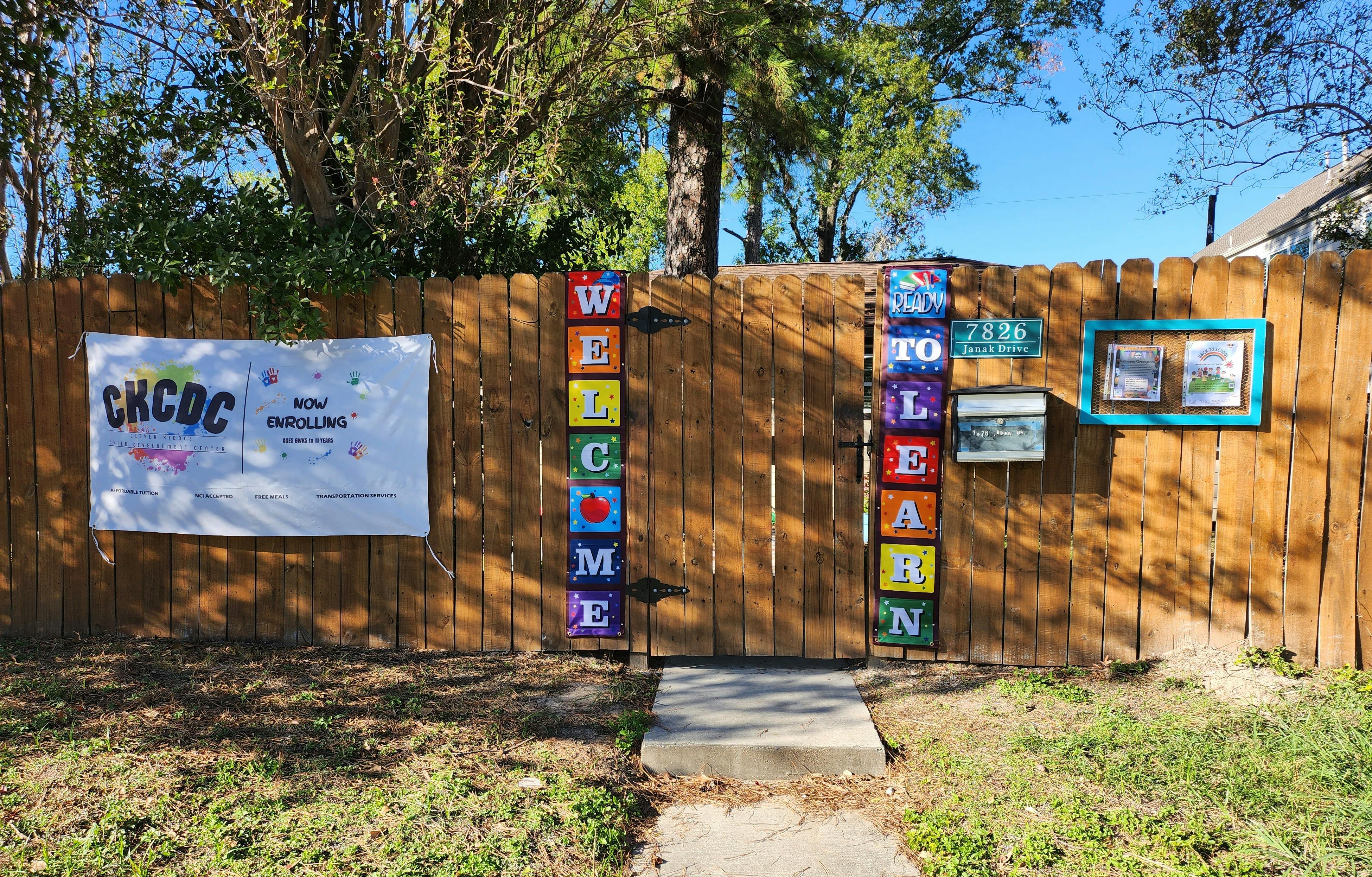 Wooden fence with a gate, a white banner, and colorful welcome signs