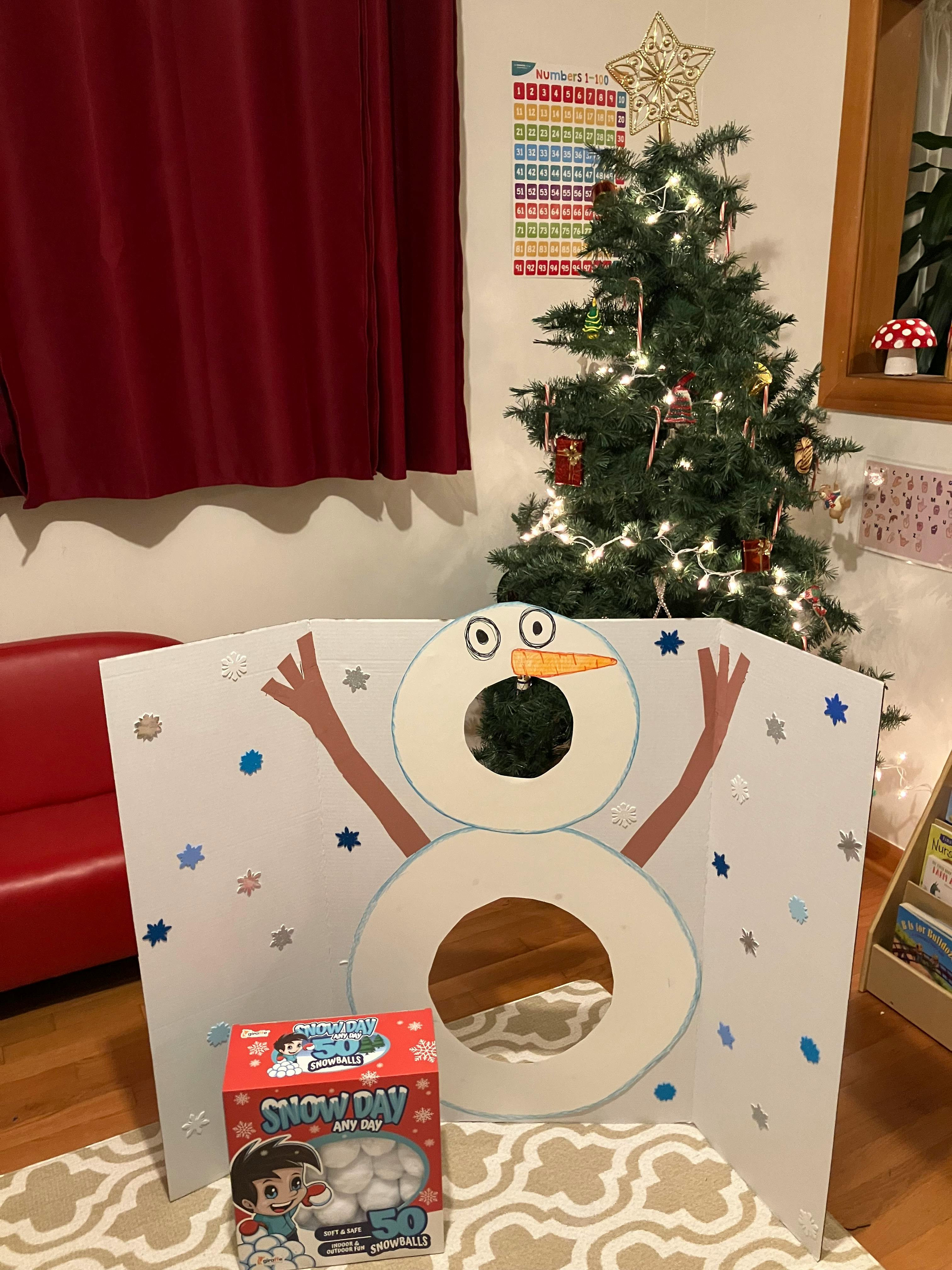 Snowman cutout with holes for a game, next to a Christmas tree