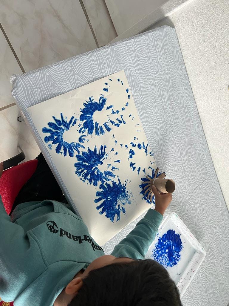 Child making blue flower prints on paper with a cardboard tube
