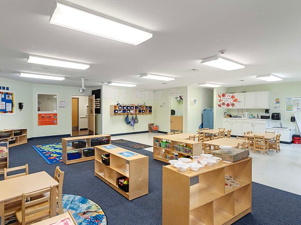 Classroom with small tables and chairs, cubbies, and an activity rug