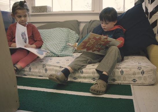 Two children sitting on a couch reading books