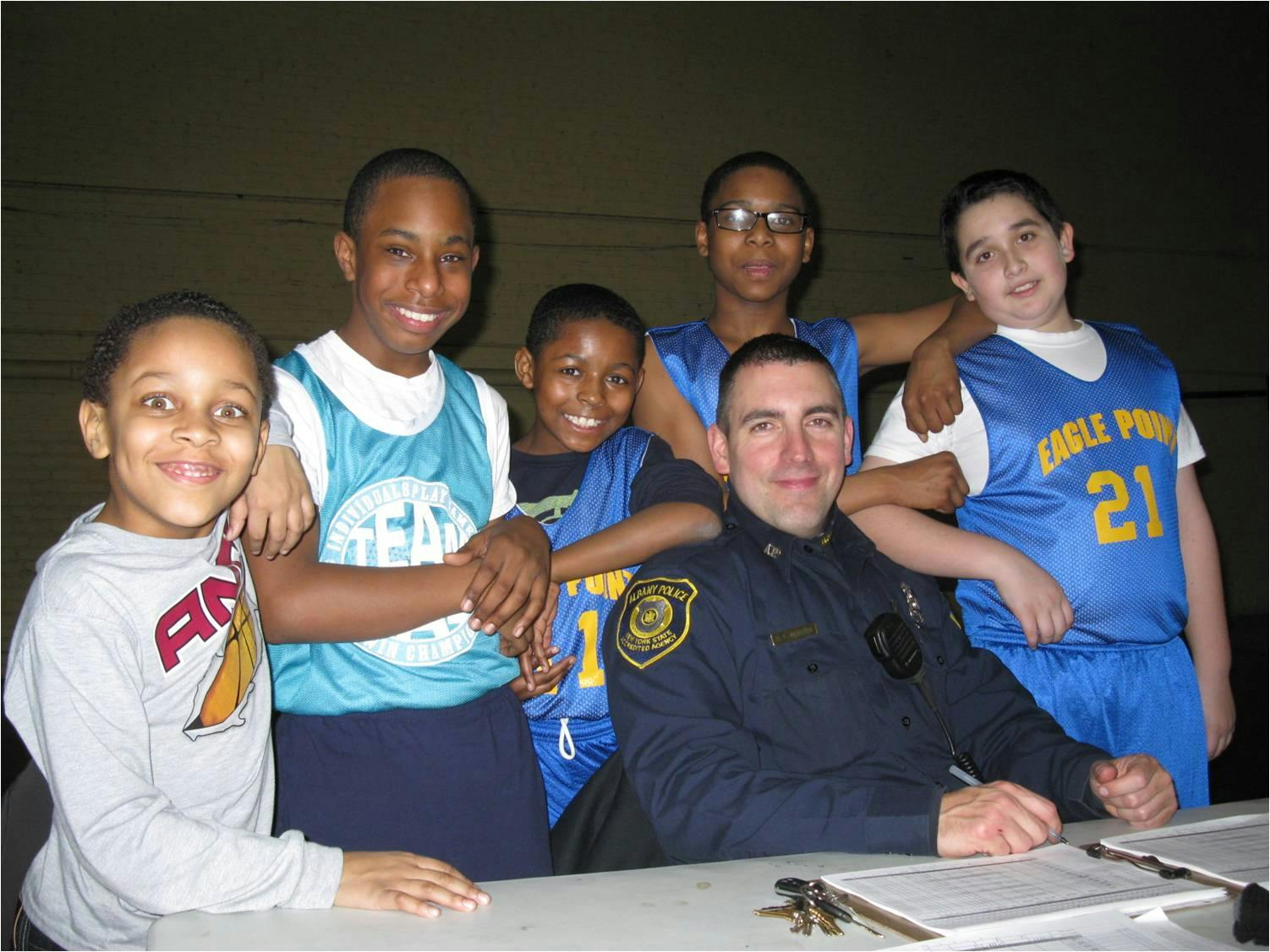 Adult in uniform with five children, some in basketball jerseys