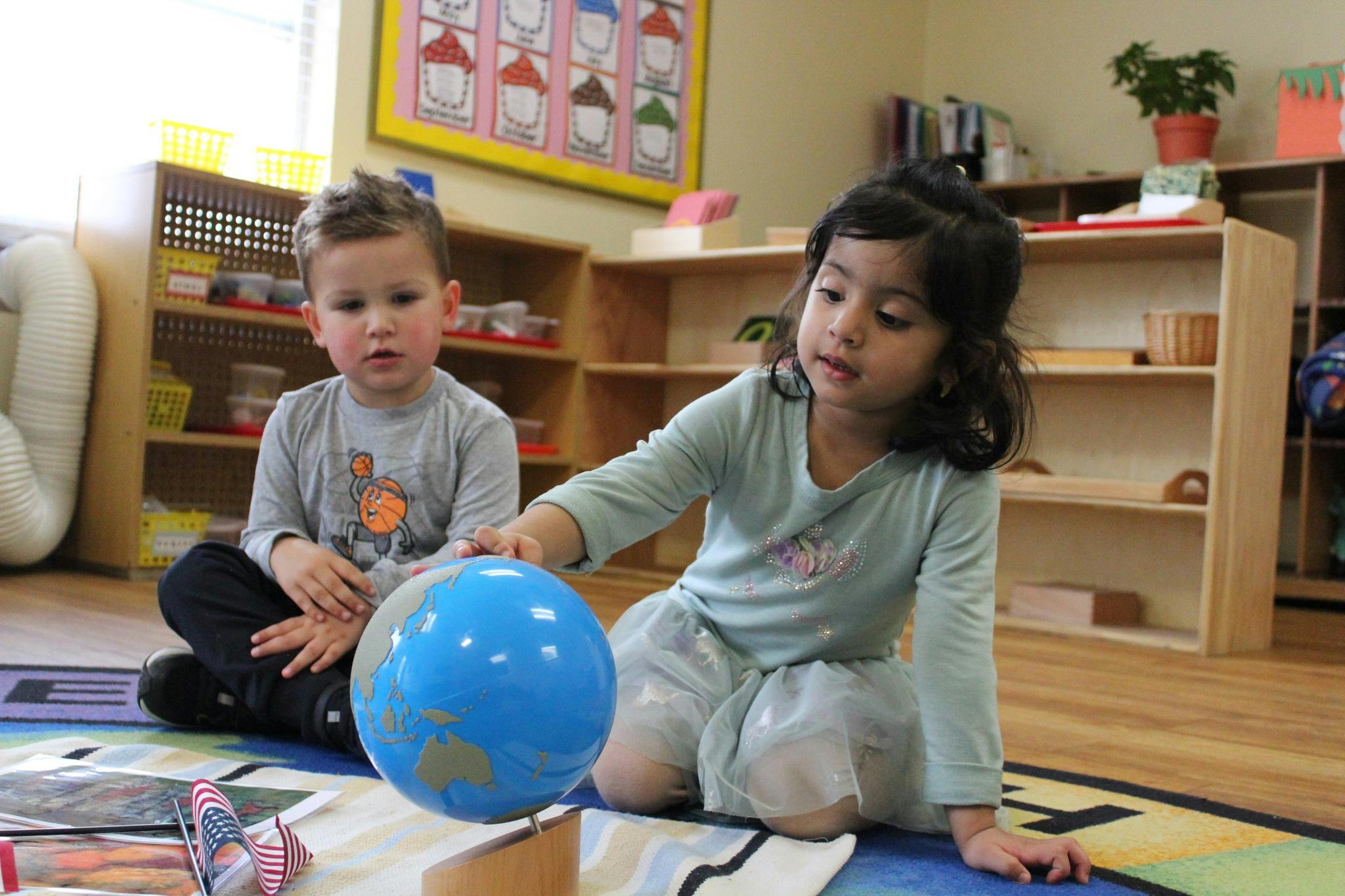 Two children on floor with a globe in a classroom