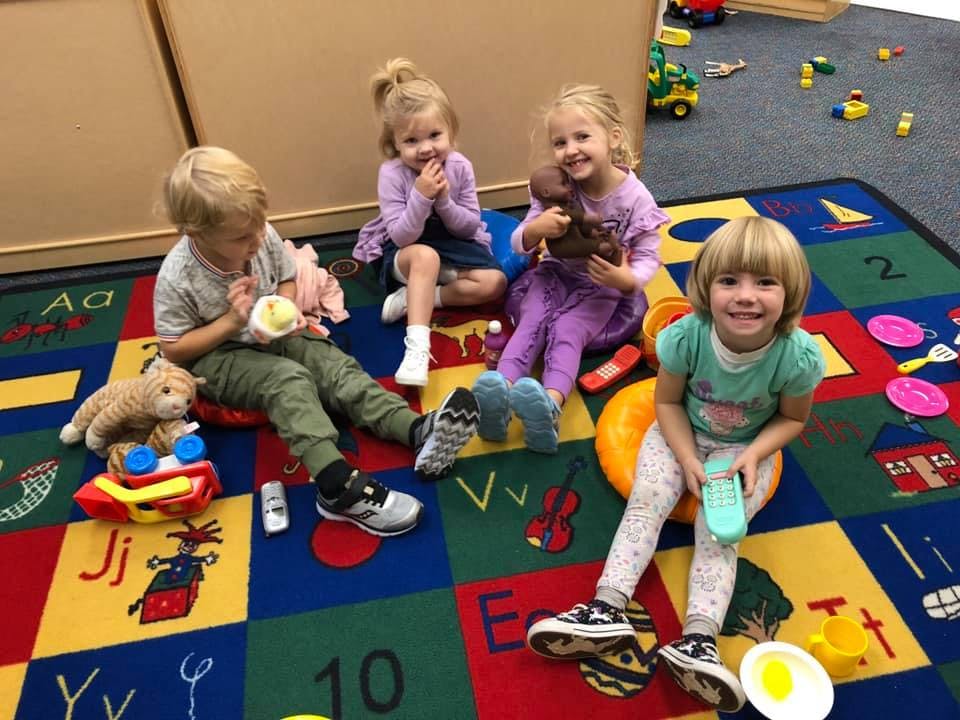 Four children playing with toys on a colorful alphabet rug