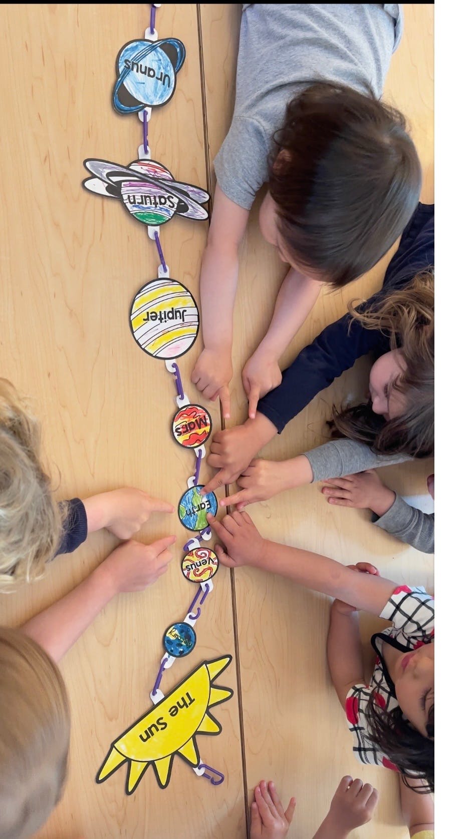 Children pointing at a paper solar system model on a table