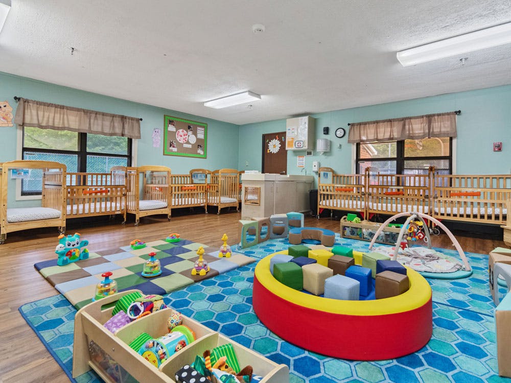A colorful childcare room with several wooden cribs and play mats