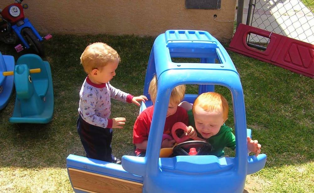 Three children playing with a toy car outdoors