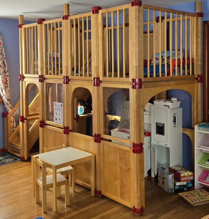 Play structure made of light wood with red connectors, including a top level and stairs