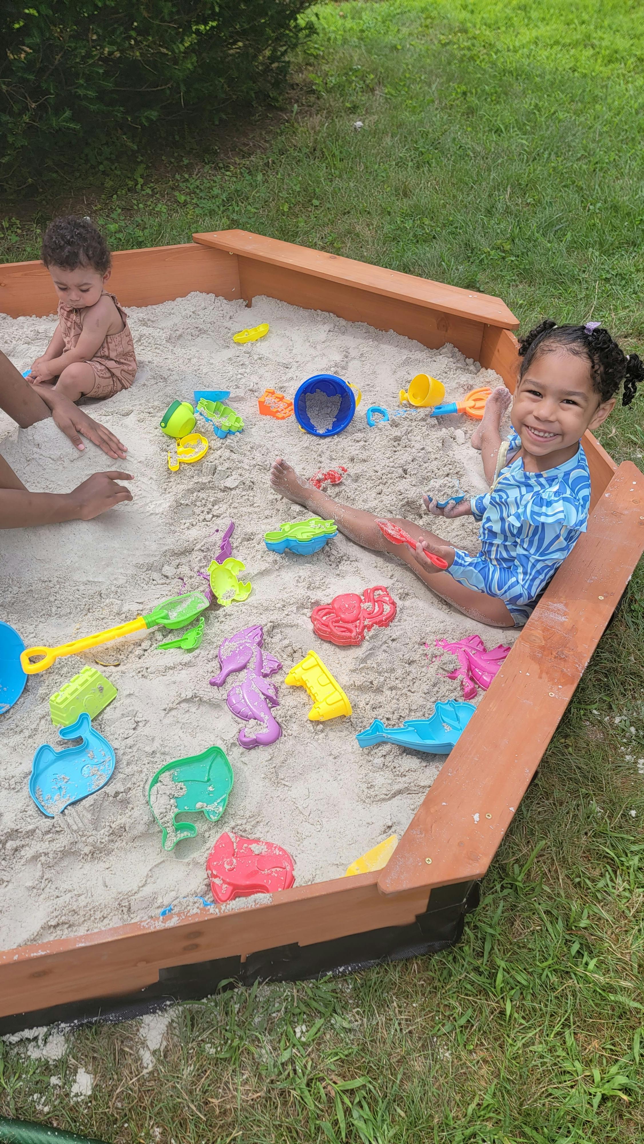 Two children playing in a sandbox with colorful toys