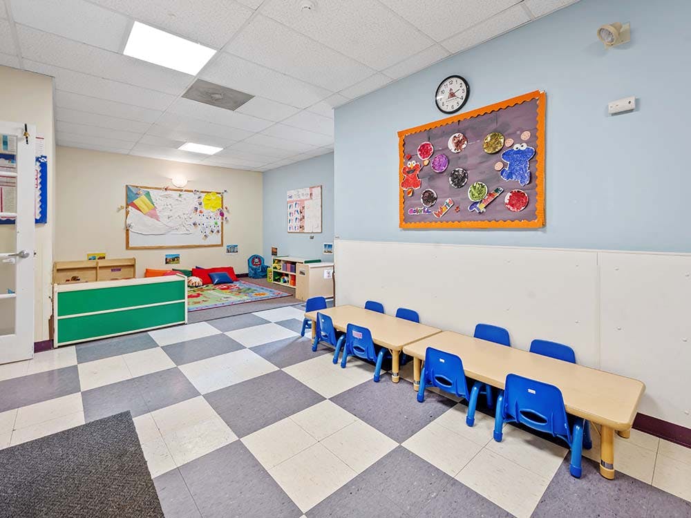 Classroom with small tables and chairs, a play rug, and colorful decorations