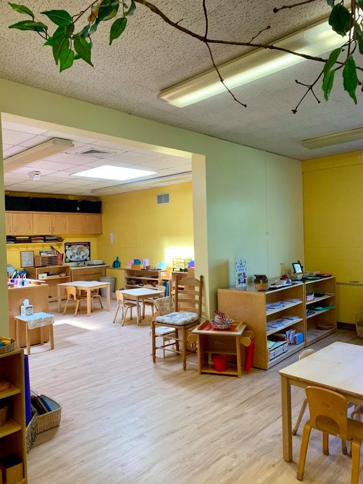Classroom with small tables and chairs, shelves with learning materials