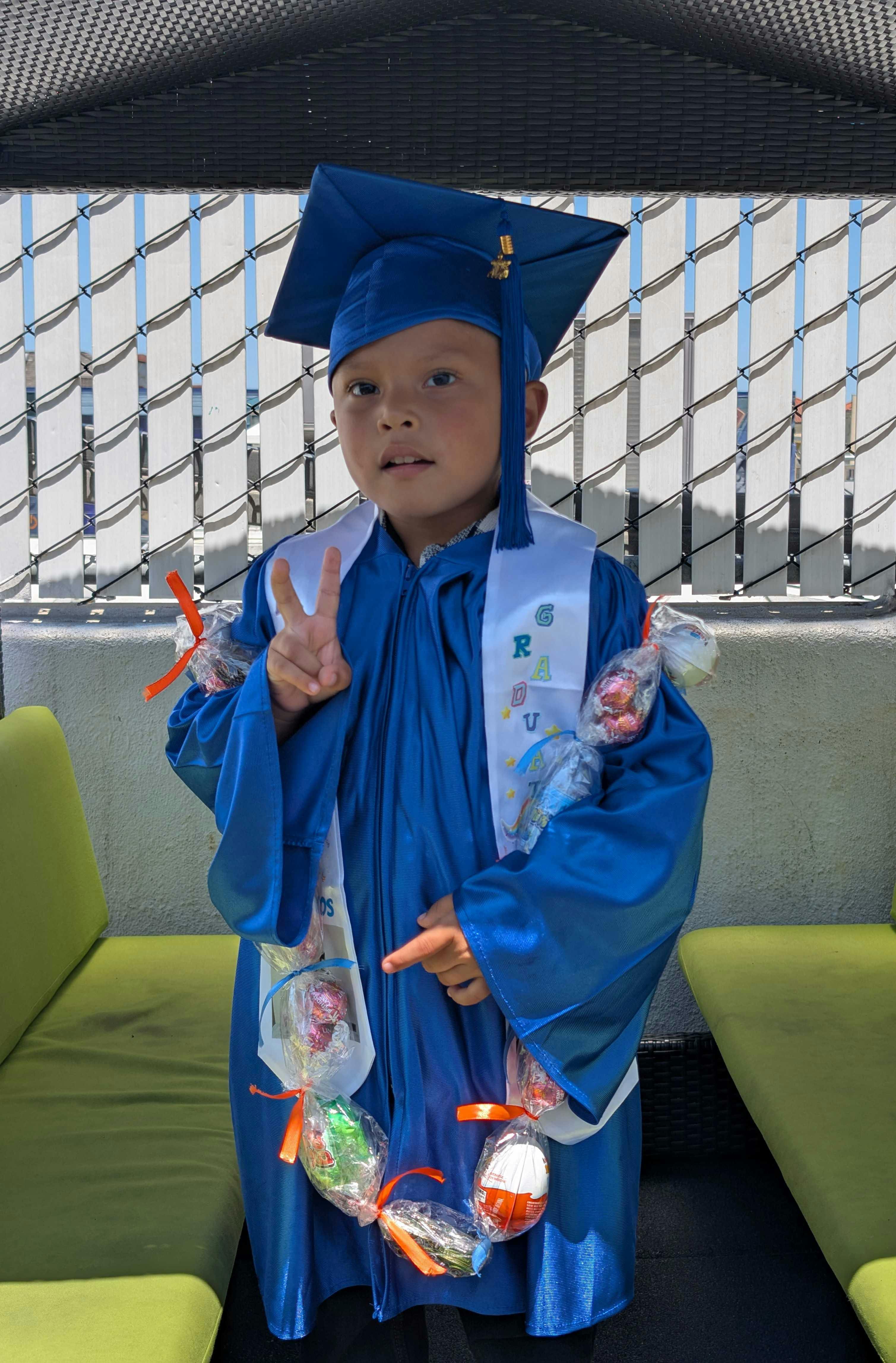 Child in blue graduation cap and gown making a peace sign