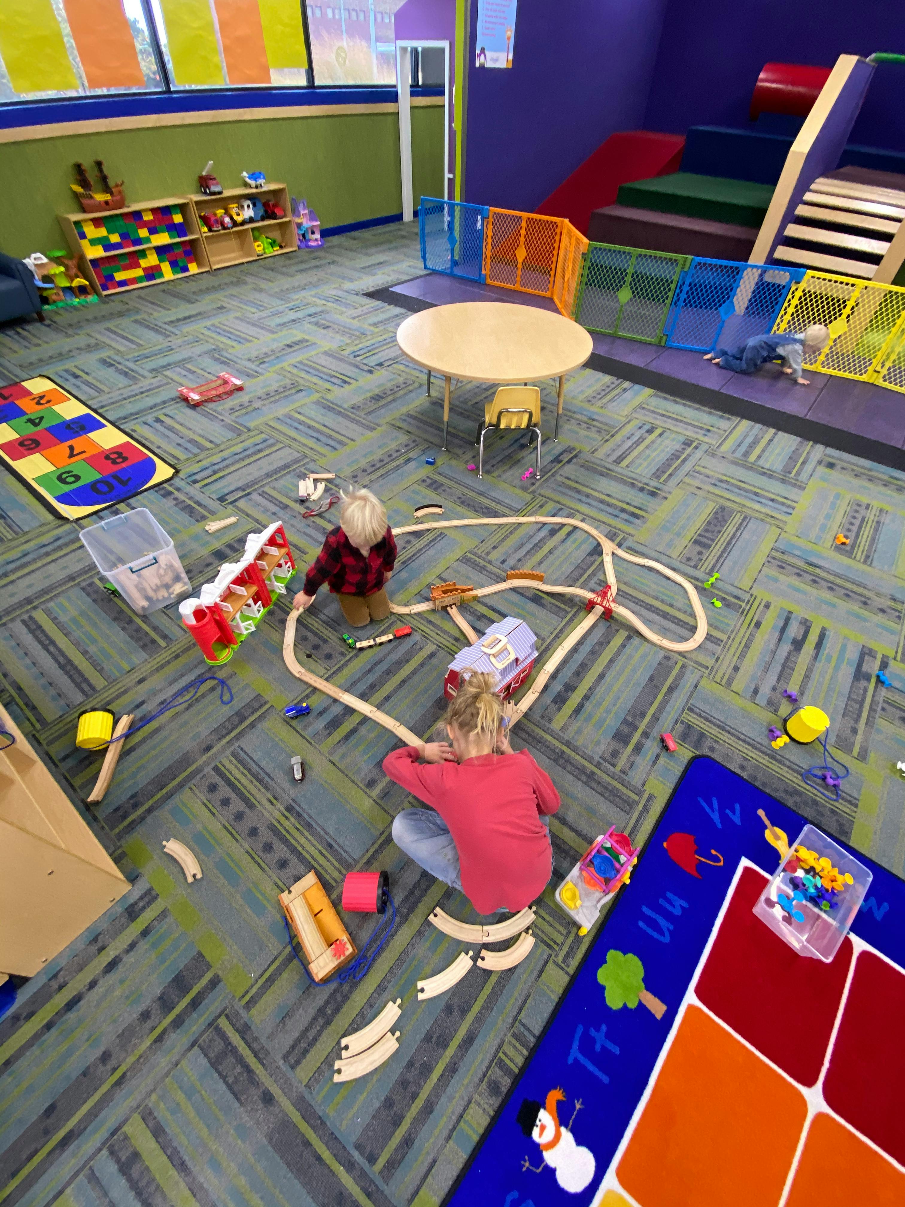 Two children playing with a wooden train set on a carpeted floor
