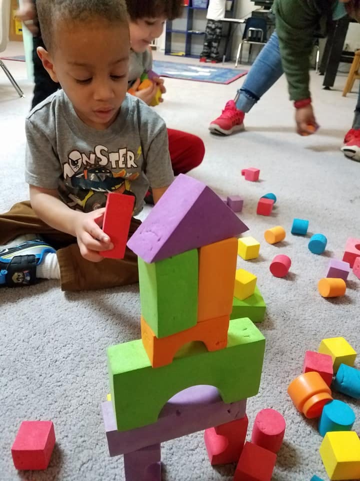 Child playing with colorful building blocks on a carpeted floor