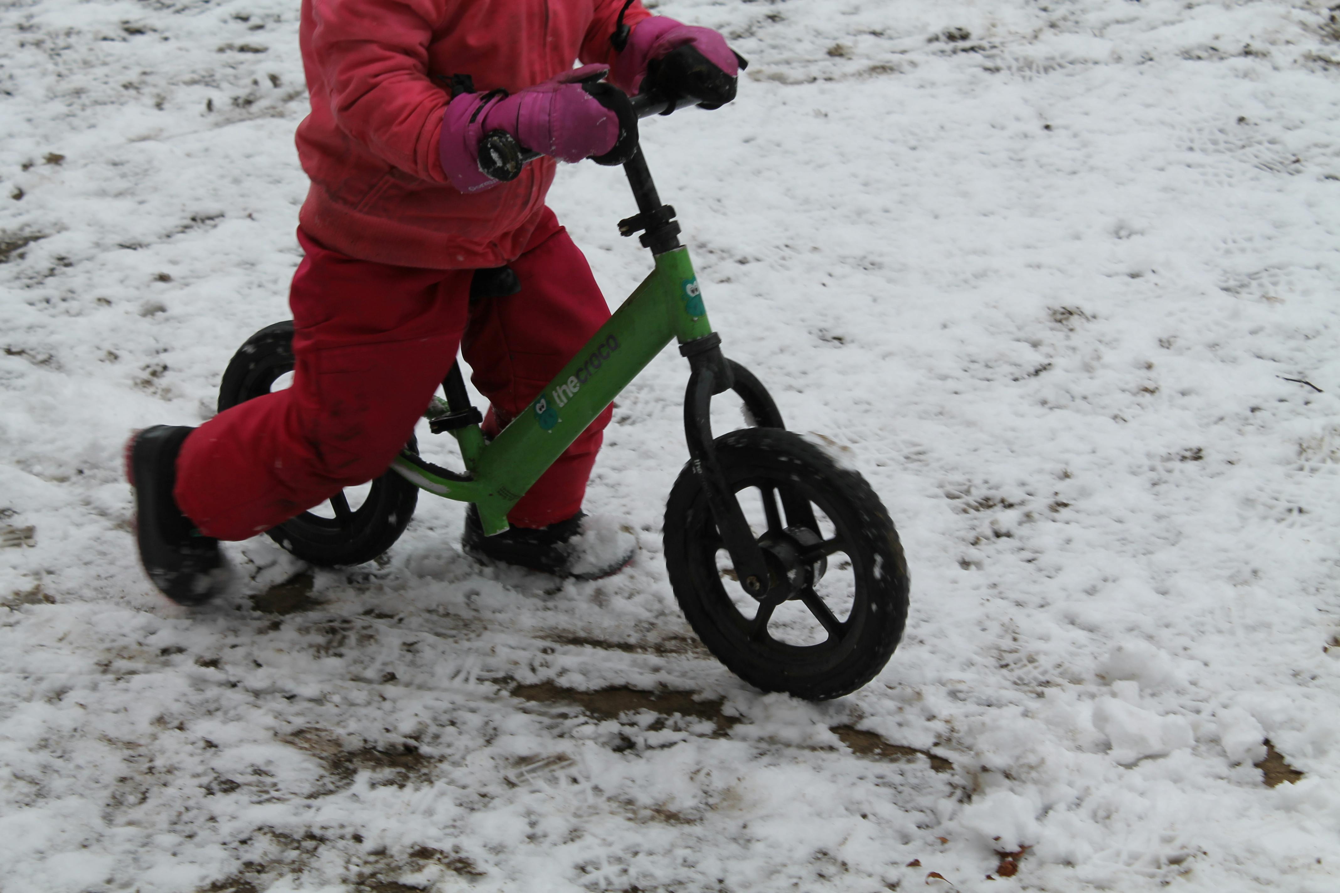 Child on a green balance bike in the snow