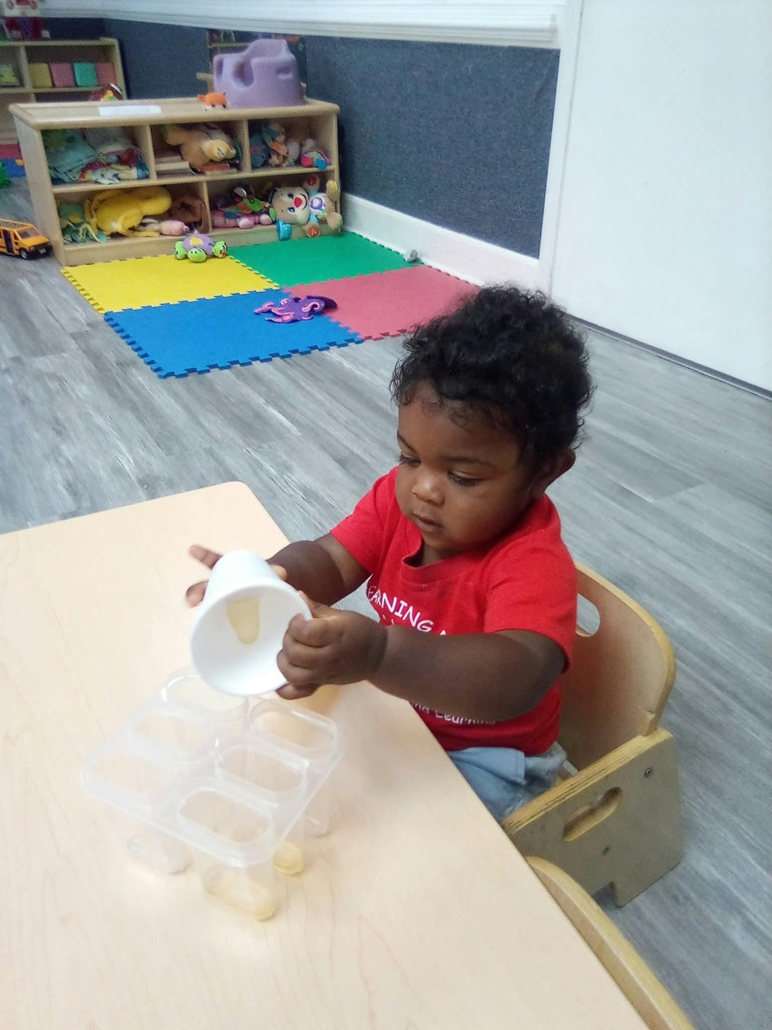 Child pouring from a cup into a clear container at a table