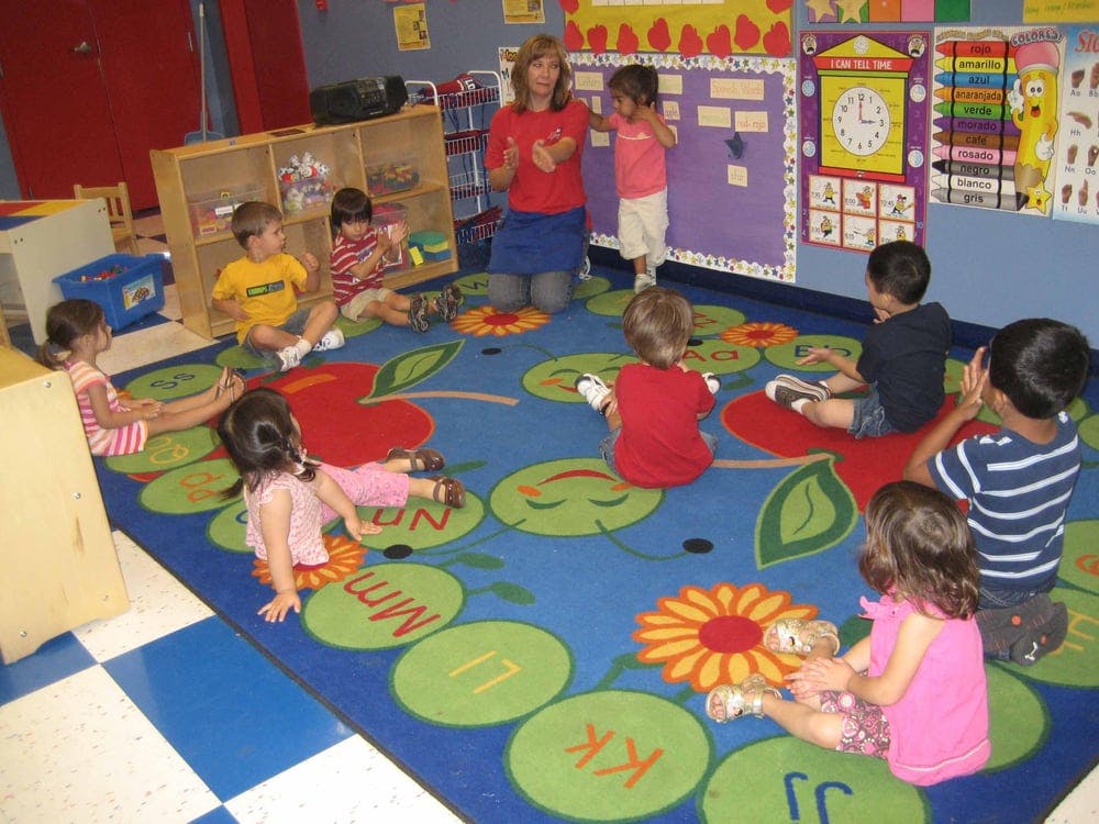 Adult and children sitting on a colorful rug in a classroom