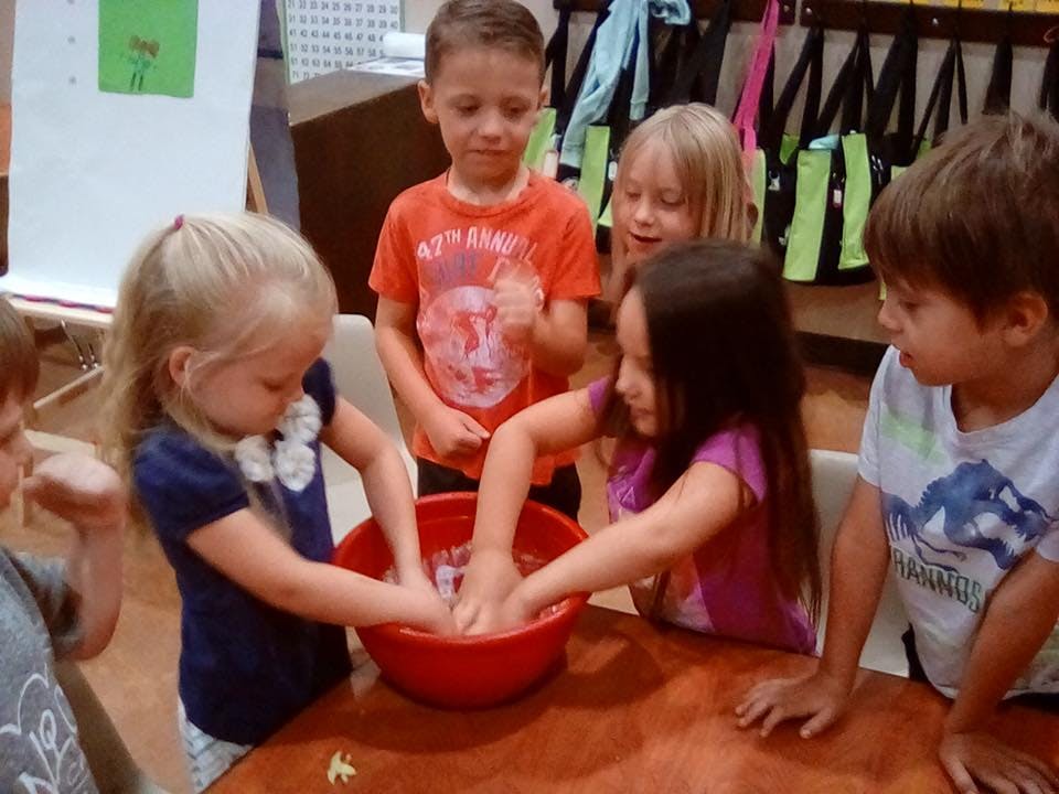 Children gathered around a red bowl with their hands in it