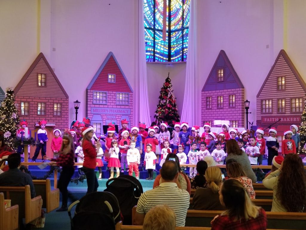 Children performing on a stage with house backdrops and Christmas trees