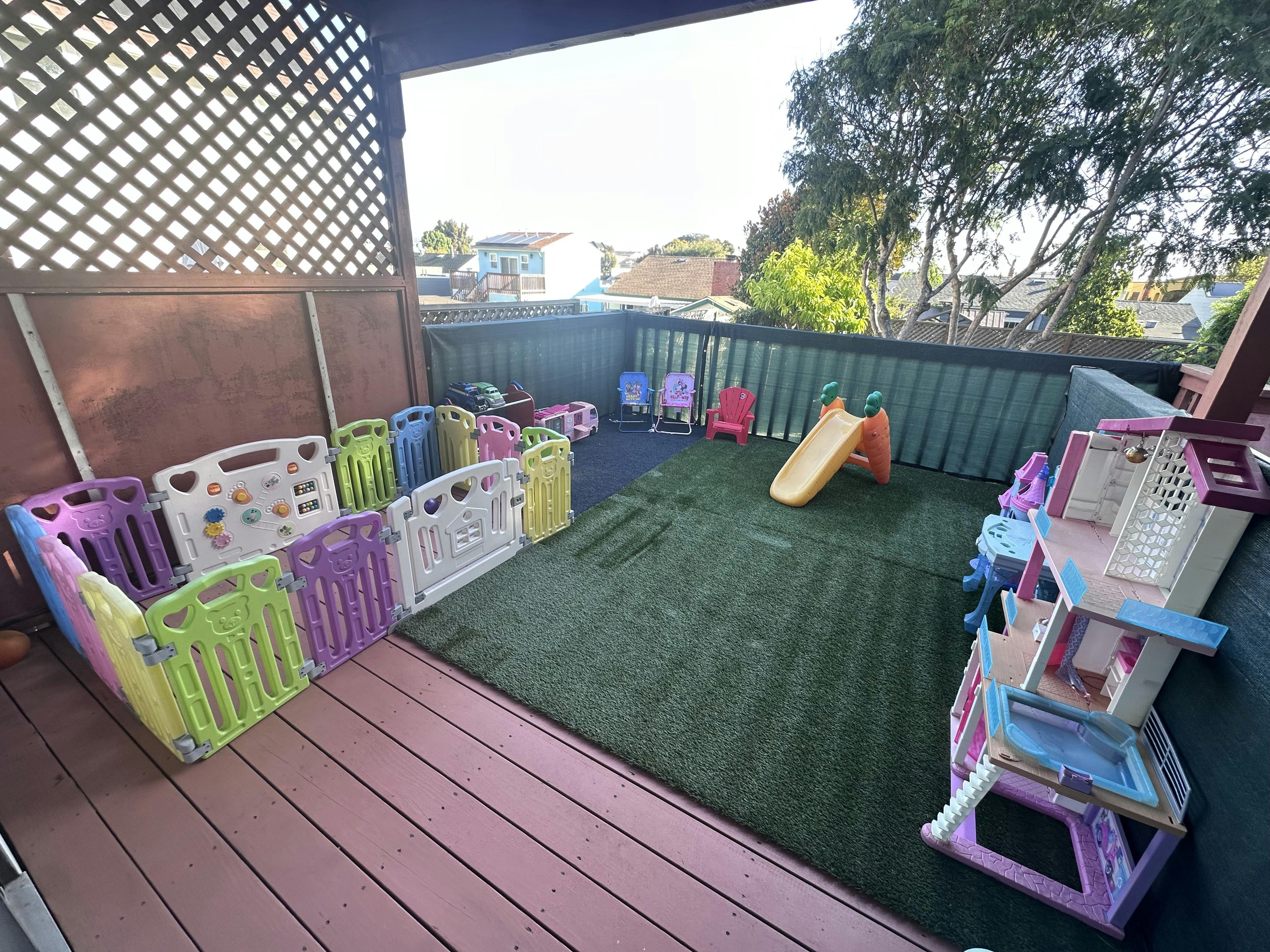 Outdoor balcony play area with a plastic playpen, small slide, and dollhouse
