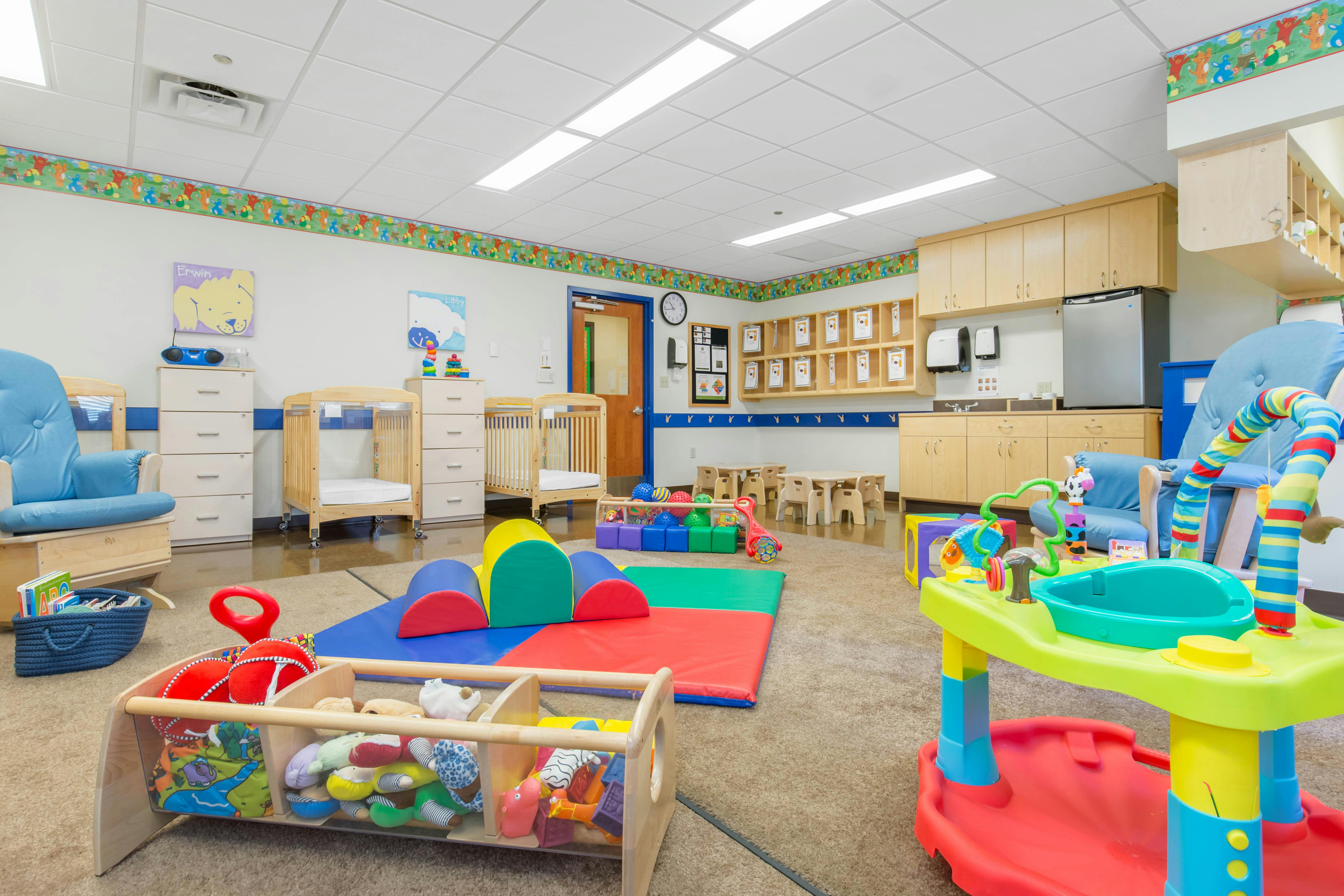 Colorful playroom with play mats, soft climbing blocks, and cribs