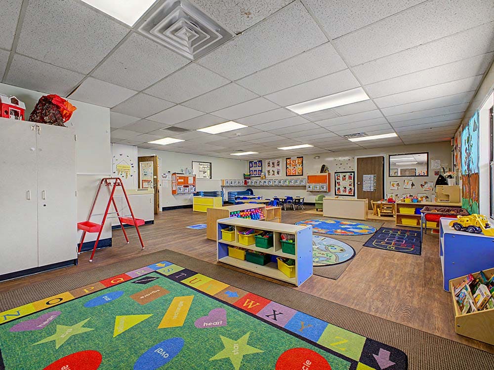 Empty colorful preschool classroom with play rug, shelves, and tables